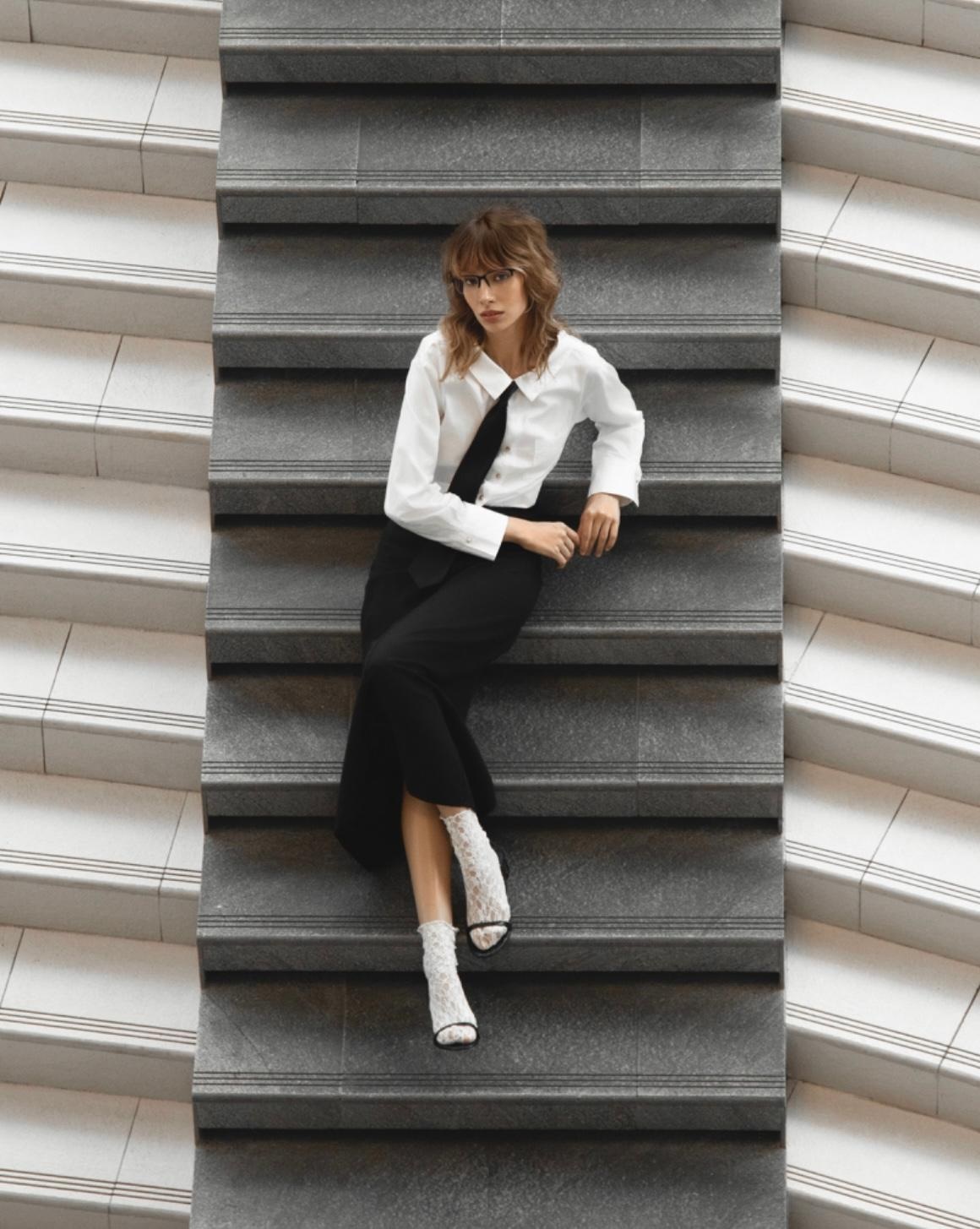 Model in a white shirt and black skirt posed on stone stairs