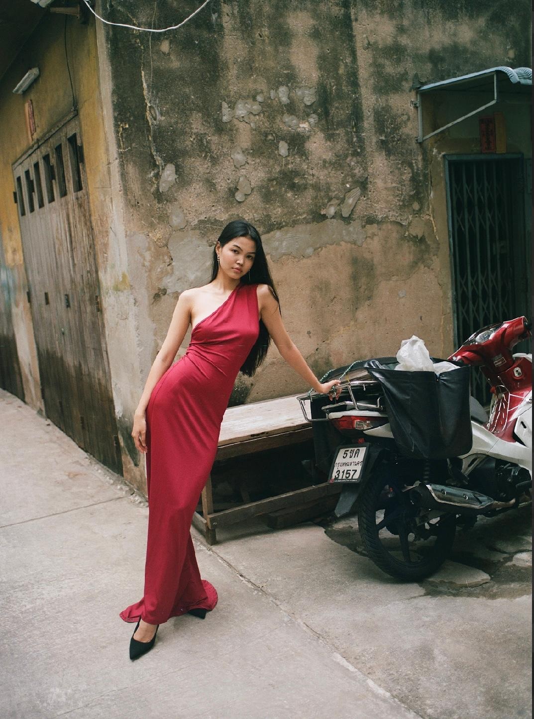 Model in a long red gown standing in a weathered city lane